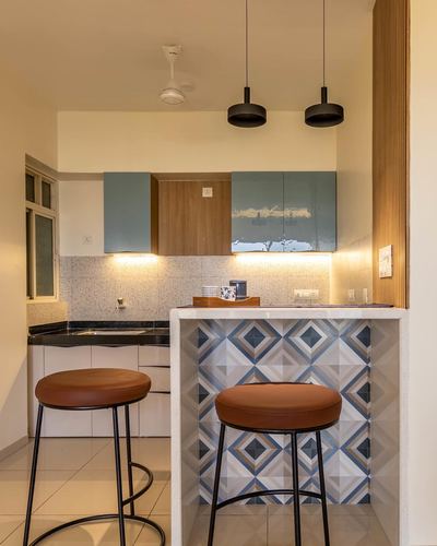 Kitchen counter with patterned tile cladding, two tan leather stools, and blue-grey glossy overhead cabinets