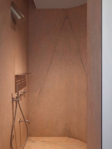 Shower niche with veined stone walls and brushed metal fixtures, warm terracotta tones