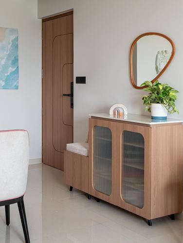 Foyer with wood-panelled door, glass-front cabinet, organic mirror and potted plant
