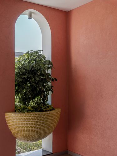 Arched niche in terracotta plaster wall holding a mosaic bowl planter with greenery