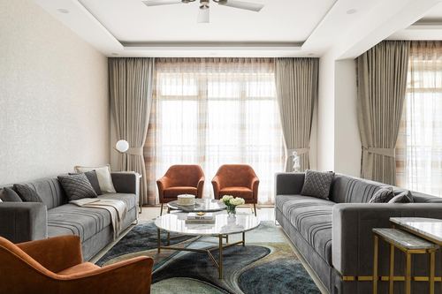Living room with two gray velvet sofas, rust leather chairs, round marble coffee table and patterned rug