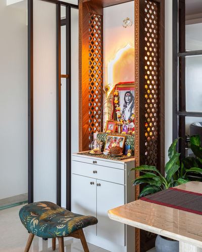 Backlit wooden jaali pooja unit with deity photo beside a teal floral stool