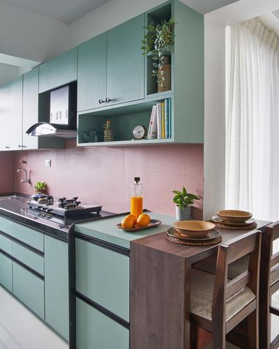 Sage green modular kitchen with pink textured backsplash and wooden breakfast counter