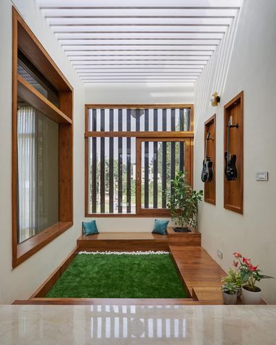 Narrow indoor passage with wooden bench, sunken artificial turf strip, and slatted skylight ceiling in a Bangalore home