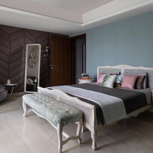 Bedroom with cane bed, blue wall, chevron fabric panelling and tufted floral bench