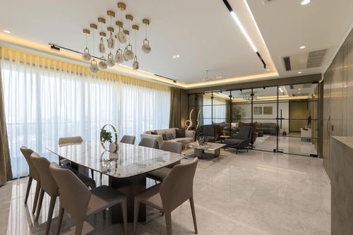 Open-plan dining and living area with marble table, tiered gold chandelier and glass partition wall