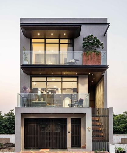 Three-storey grey minimalist house facade at dusk with glass balconies and warm interior light