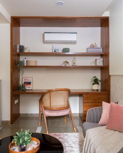 Wood-toned built-in study nook with open shelves, desk, and cane chair with pink cushion