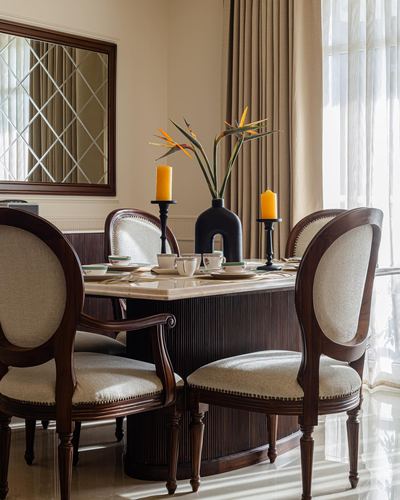 Formal dining table with oval-back chairs, marble top, and bird of paradise centerpiece near curtained window