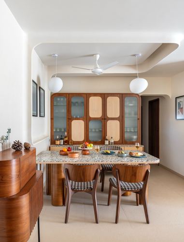 Dining area with terrazzo table, teak chairs, and curved wooden crockery cabinet under a cove ceiling