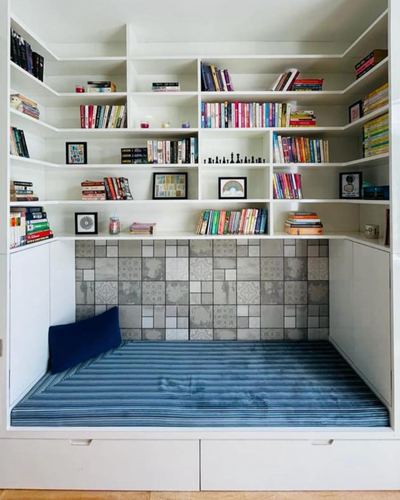 White built-in bookshelf niche with patterned grey tile and a blue striped window seat below