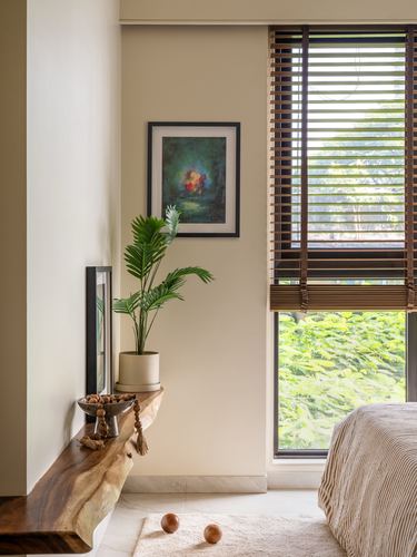 Bedroom corner with live-edge wood shelf, framed artwork, plant, and striped bed by a window with wooden blinds