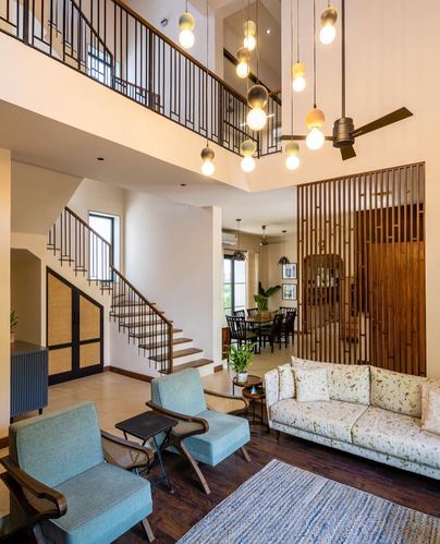 Double-height living room with staircase, pendant lights, wood slat screen and floral sofa