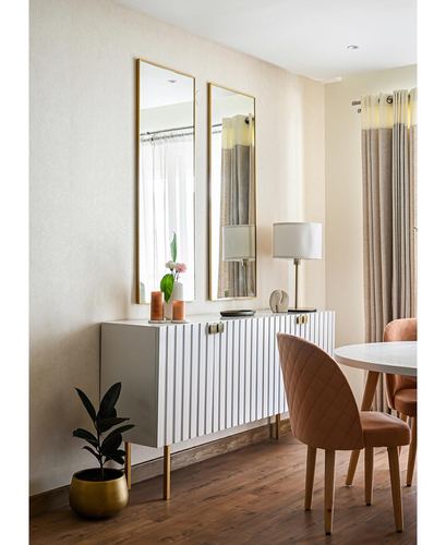 Fluted white sideboard with brass legs under two tall gold mirrors beside dining table