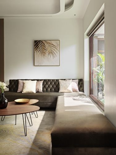 Sunlit living room with olive tufted sofa, wooden coffee tables, and leaf artwork above