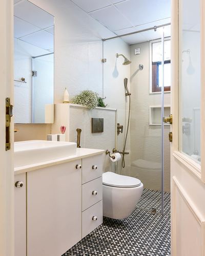 White bathroom with vessel sink, wall-hung toilet, glass shower and patterned black-and-white floor tiles