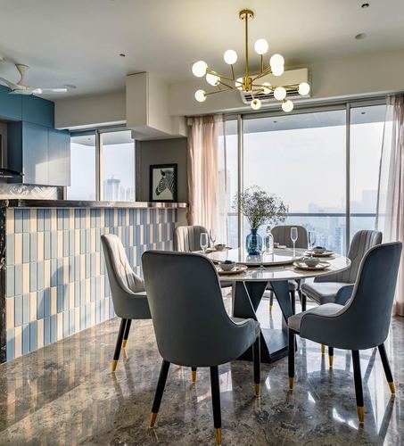 Round marble dining table with grey velvet chairs beneath a brass sputnik chandelier facing city skyline