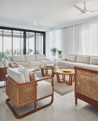 Ivory living room with cane armchairs, wooden sofas, brass coffee tables and sheer curtains by tall windows