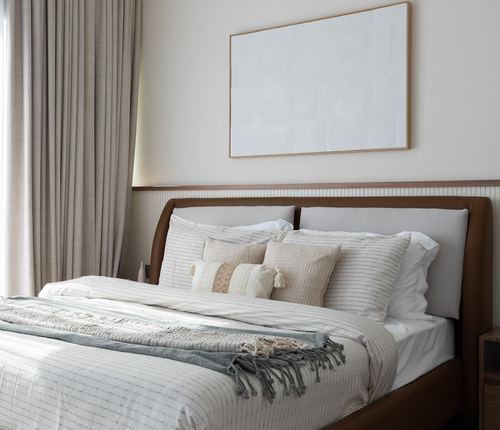 Neutral bedroom with wood-trimmed upholstered headboard, layered pillows, and abstract art above