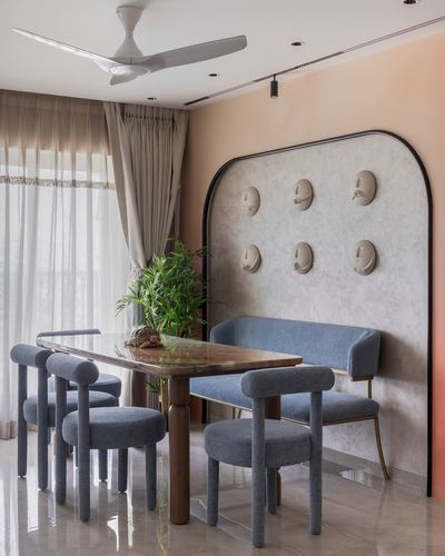 Dining room with wooden table, blue bouclé chairs and bench against an arched plaster wall with face sculptures