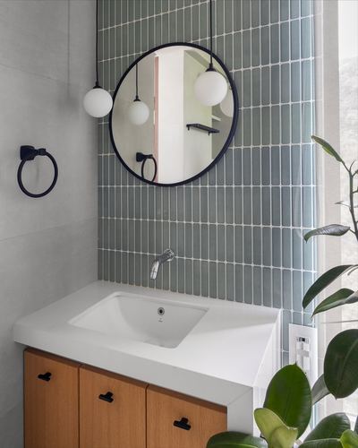 Bathroom vanity with round mirror, globe pendant lights and green tiled wall, wood cabinet below.