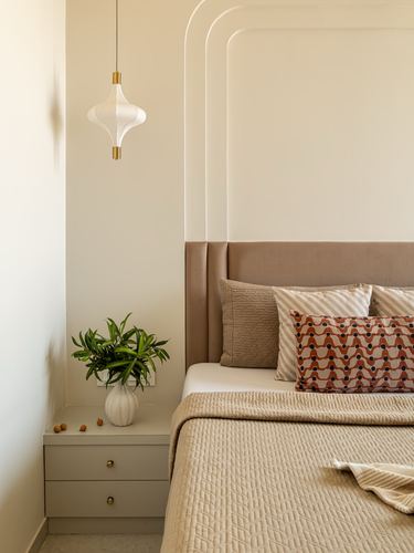 Beige bedroom with arched headboard wall, pendant light, and rust-patterned throw pillows