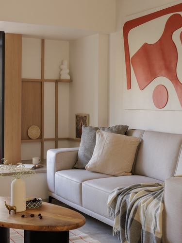 Beige sofa with cushions beneath a red abstract artwork, wooden partition nook to the left