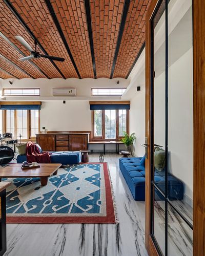 Living room with vaulted brick ceiling, blue velvet sofas, patterned rug, and steel-glass partition.