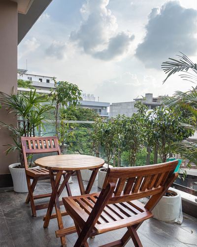 Balcony with wooden folding chairs, round table, and potted plants overlooking a cloudy urban skyline