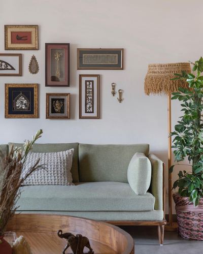 Sage green sofa beneath an eclectic gallery wall with a fringed floor lamp and potted plant
