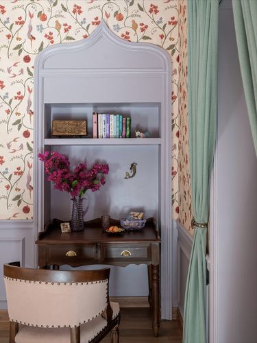 Lavender arched niche with bookshelf and wooden desk against floral wallpaper, sage curtain beside