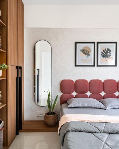 Bedroom with pink scalloped headboard, oval mirror, wooden wardrobe and botanical prints on textured wall