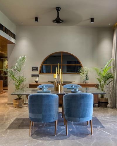 Dining table with blue velvet chairs facing a wood-framed arched mirror above a console