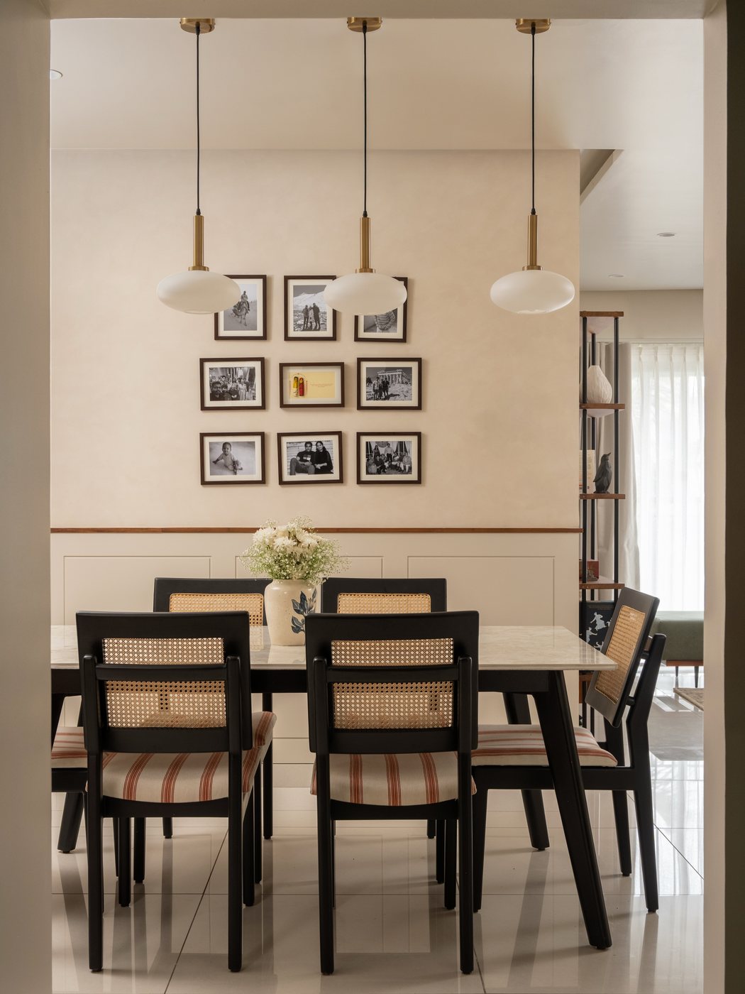 Dining room with cane-back chairs, marble-top table, and a gallery wall of framed photos under pendant lights