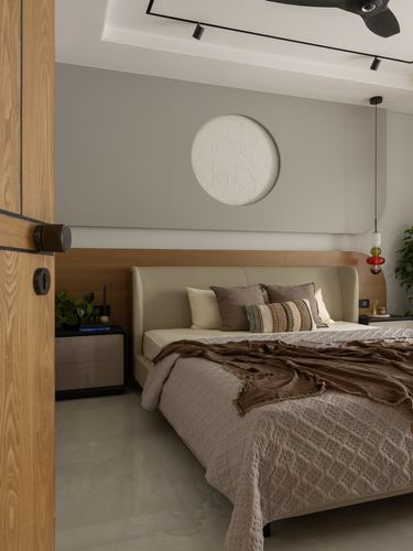 Bedroom with curved beige headboard, wood paneled wall, round textured wall art, and layered bedding