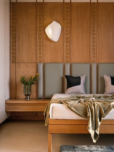 Wood-panelled bedroom wall with sconce, floating nightstand, and bed with sage throw