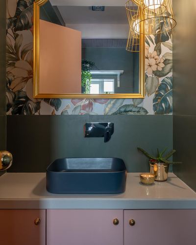 Bathroom vanity with floral wallpaper, gold mirror, dark vessel sink, pink cabinetry