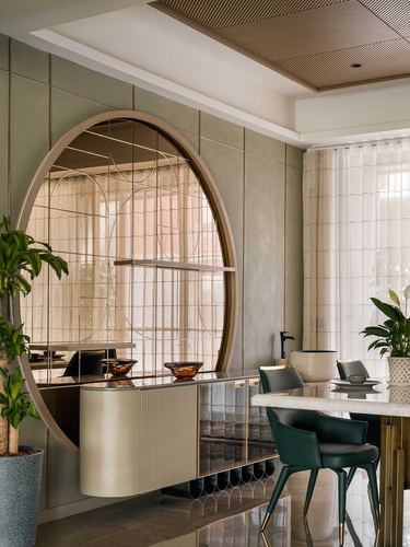 Dining area with round mirrored feature wall, fluted sideboard, marble table and green leather chairs