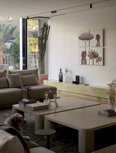 Neutral living room with layered coffee tables, taupe sofa, glowing stone console and four-panel artwork
