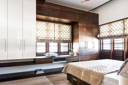 Bedroom with dark wood wardrobes, built-in window seat, and patterned roman blinds beside a bed