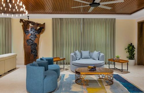 Living room with curved blue sofa, round coffee table, and carved wood wall sculpture under a wood-slatted ceiling