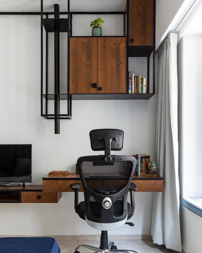 Home office corner with black mesh chair, floating wood desk, and modular black shelving with wood cabinets