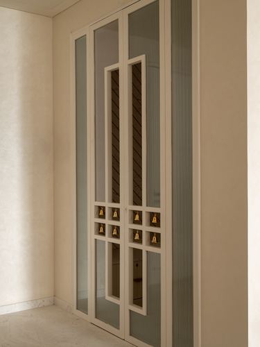 Fluted glass cabinet doors framing a mirrored pooja niche hung with small brass bells