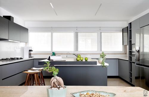 Grey and white U-shaped kitchen with central island under a row of windows, green apples and plants on counter
