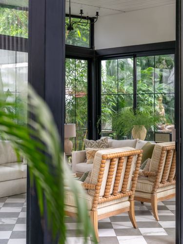Living room with spindle-back chairs, checkered floor, and black-framed windows facing greenery