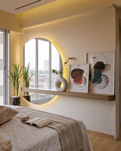 Bedroom with backlit round mirror, floating shelf styled with art and plants, city view window