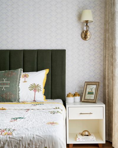 Bed with olive velvet headboard beside white nightstand and brass wall sconce