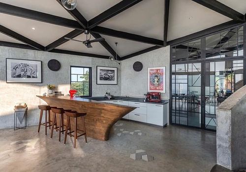 Kitchen with curved wooden bar counter under black exposed truss ceiling and glass partition wall