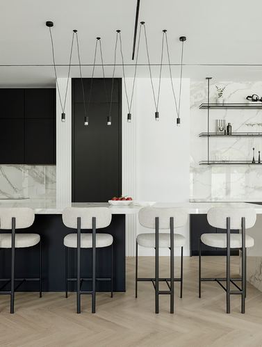 Black and white kitchen with marble backsplash, herringbone wood floor, and boucle bar stools under sculptural pendant lights
