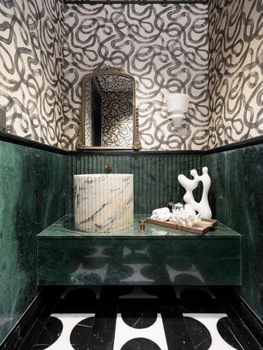 Powder room with green marble walls, swirling wallpaper, ornate mirror, and ribbed marble drum vanity.